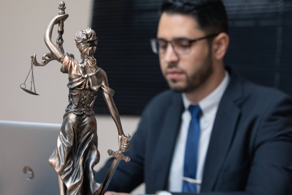 LAwyer sitting at the table with the Lady Justice statue next to him. Workers Compensation Lawyers.