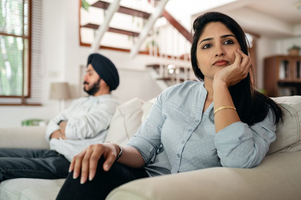 Husband and wife arguing nd sitting on the couch. The Psychosocial Impact of Hearing Loss.