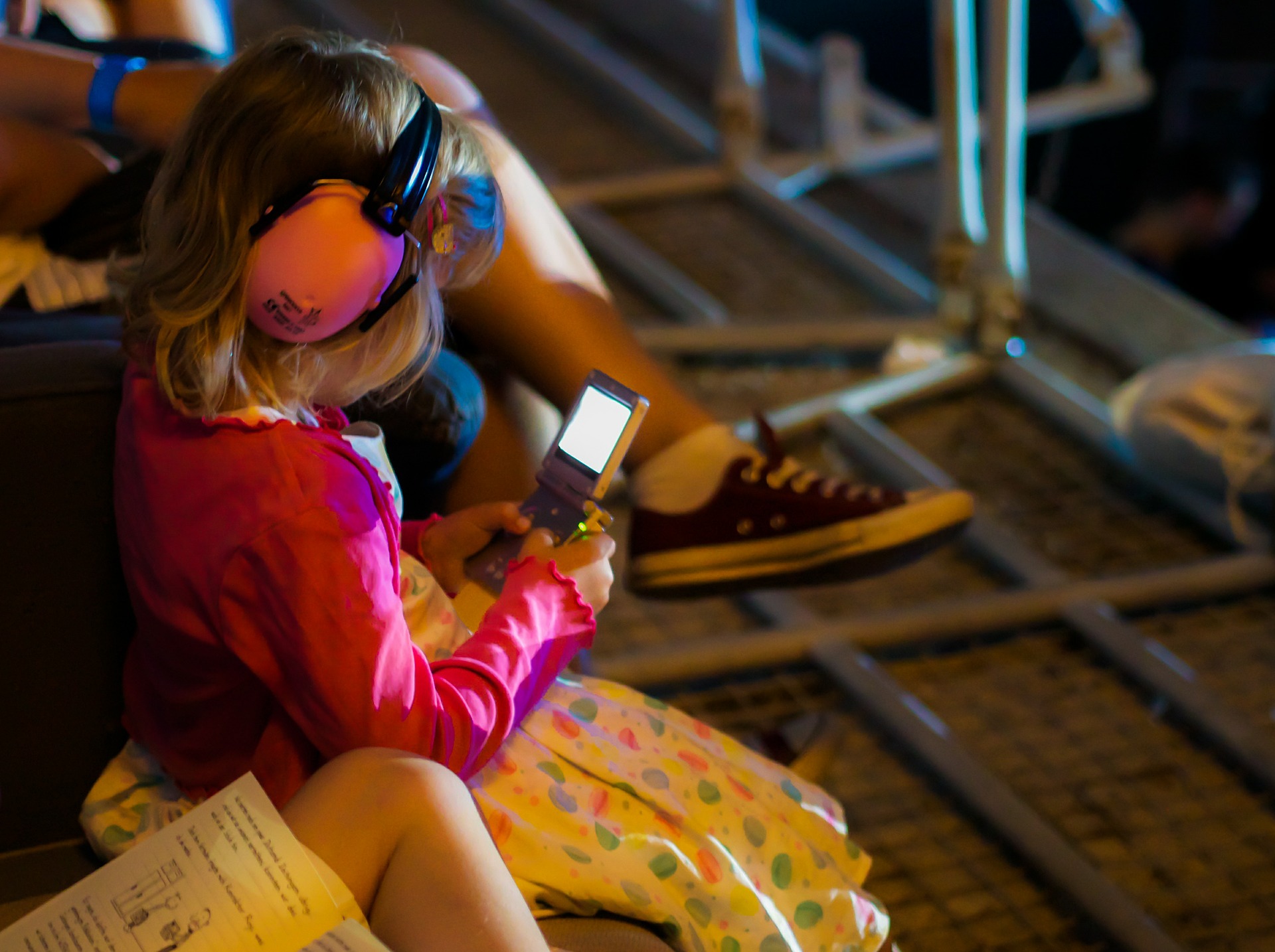 Little girl with ear muffs looking at the phone. Types of Hearing Protection