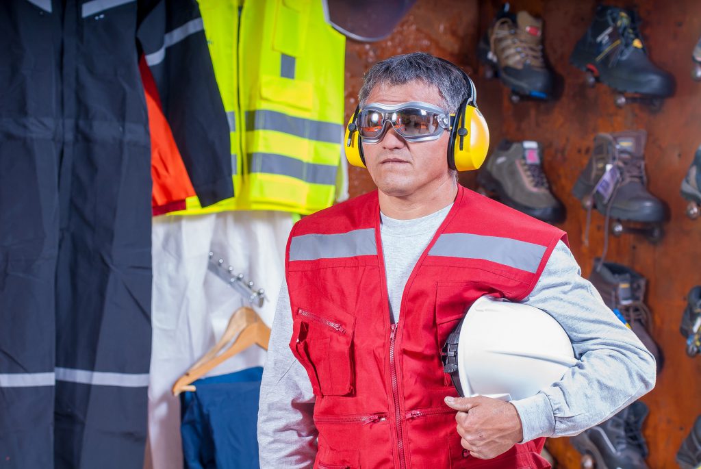 Industrial Deafness. Worker with helm under arm, googles, and hearing protection looking straight