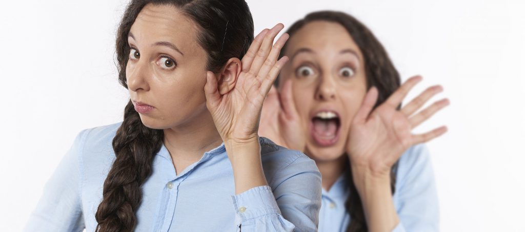 How To Improve Hearing? Woman trying to hear something with a gesticulation with a hand behind her ear while other girl yells behind her back.