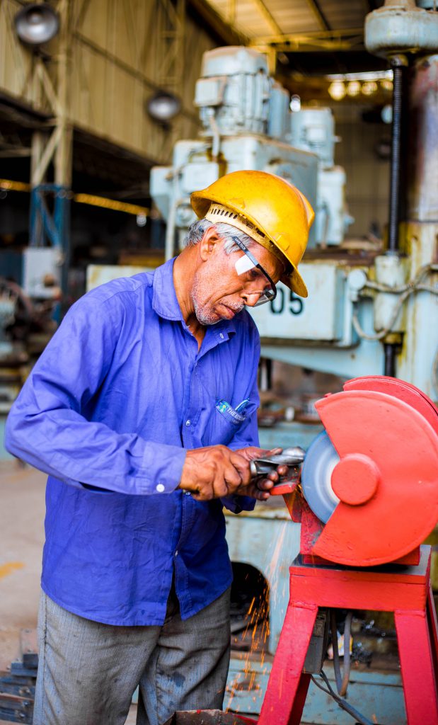 Man grinding metal part on the red grinder. Hearing Impairment in the Workplace