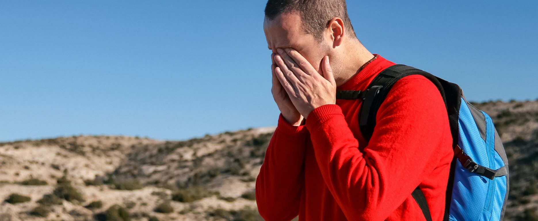 Man hiking in a red shirt having a headache